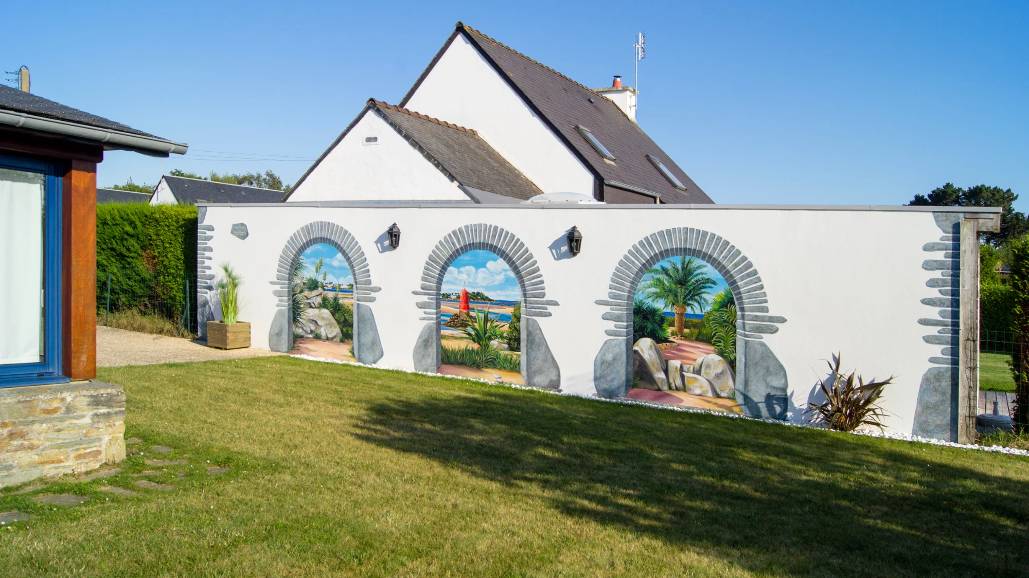 Vue large des trois arches peintes en trompe-l'œil sur le mur de jardin d'un particulier à Locquirec